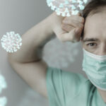 Exhausted healthcare worker in a surgical mask surrounded by floating particles, symbolizing the airborne spread of Legionnaires’ disease in healthcare settings.