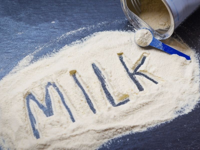 Milk powder with a scoop spilled on a dark surface, word ‘MILK’ written in powder – representing the best breast milk increasing powders buying guide for lactating mothers