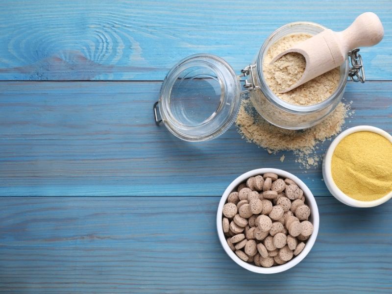 Various forms of brewer's yeast including powder and tablets, often used as a breast milk increasing powder for lactating mothers, displayed on a blue wooden table