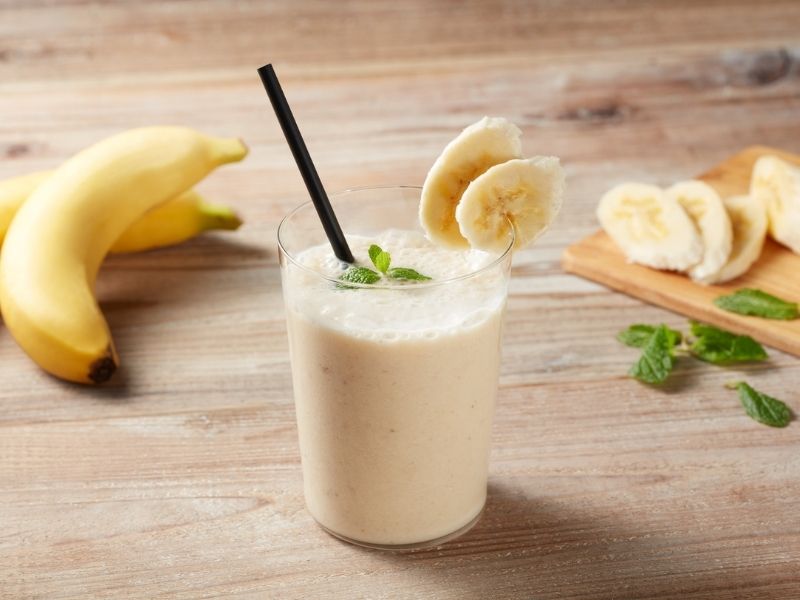 Homemade banana smoothie in a glass with mint and sliced bananas on wooden table – DIY recipe idea with breast milk increasing powder for lactating mothers